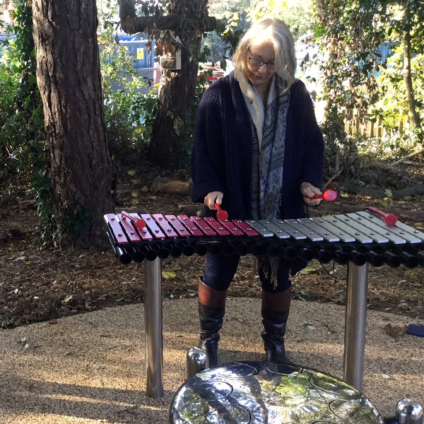 lady with grey hair playing a pin and silver large outdoor xylophone in the Aldeburgh hospital Sensory Garden