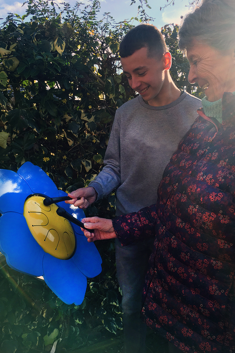 a grandmother and grandson playing on an outdoor drum shaped like a forget me not flower in a sensior care home