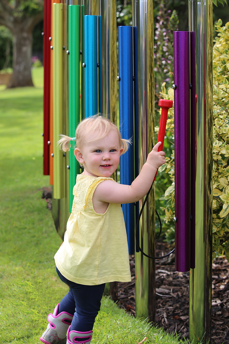 a young girl playing rainbow coloured musical chimes in a school playground