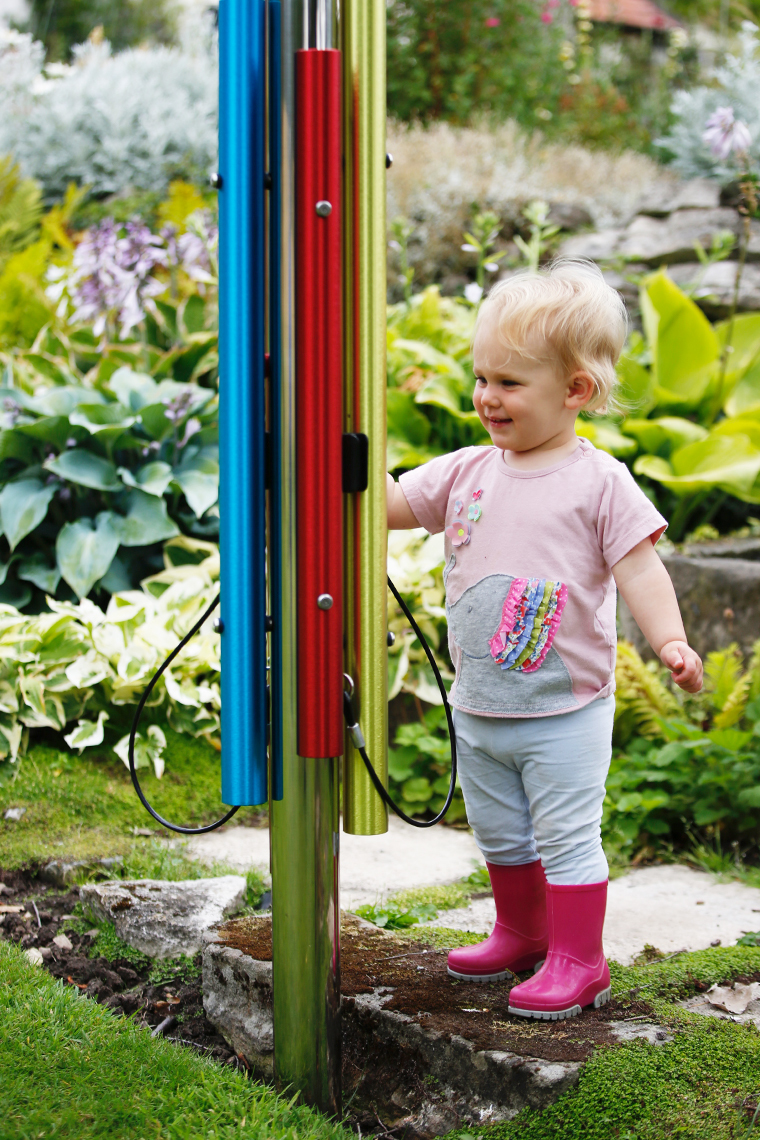 little blonde boy playing an outdoor rainbow chime post in a musical playground