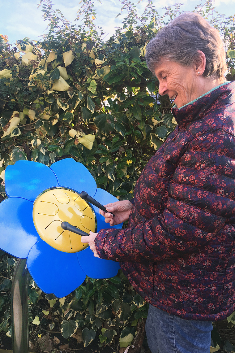 older lady playing a colorful outdoor drum shaped like a forget me not flower in a senior living center