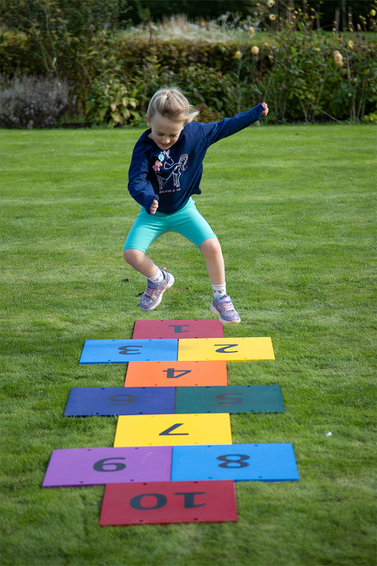 a young girl jumping on an outdoor colourful musical hopscotch installed in grass