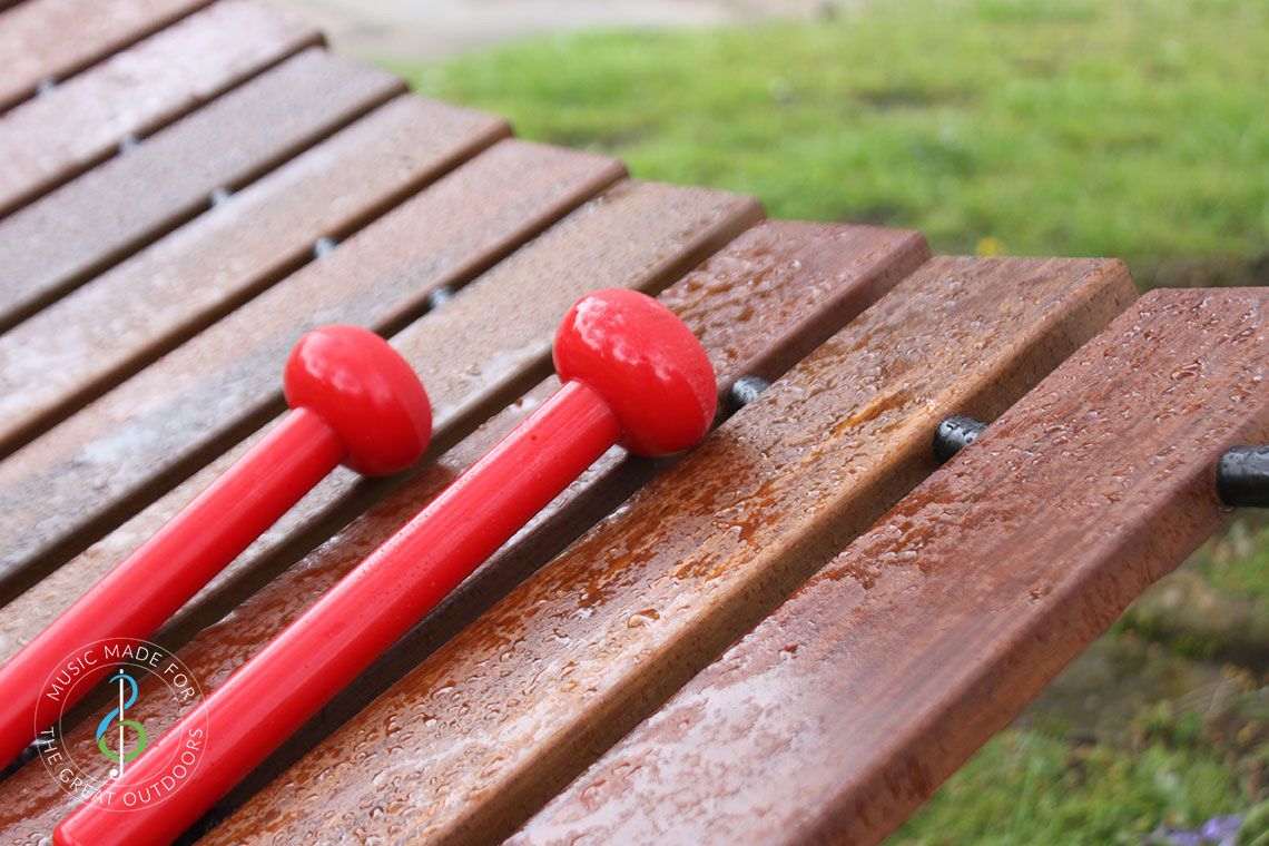 image of a Large Outdoor Playground Akadinda Xylophone with red beaters With Raindrops on the wooden notes