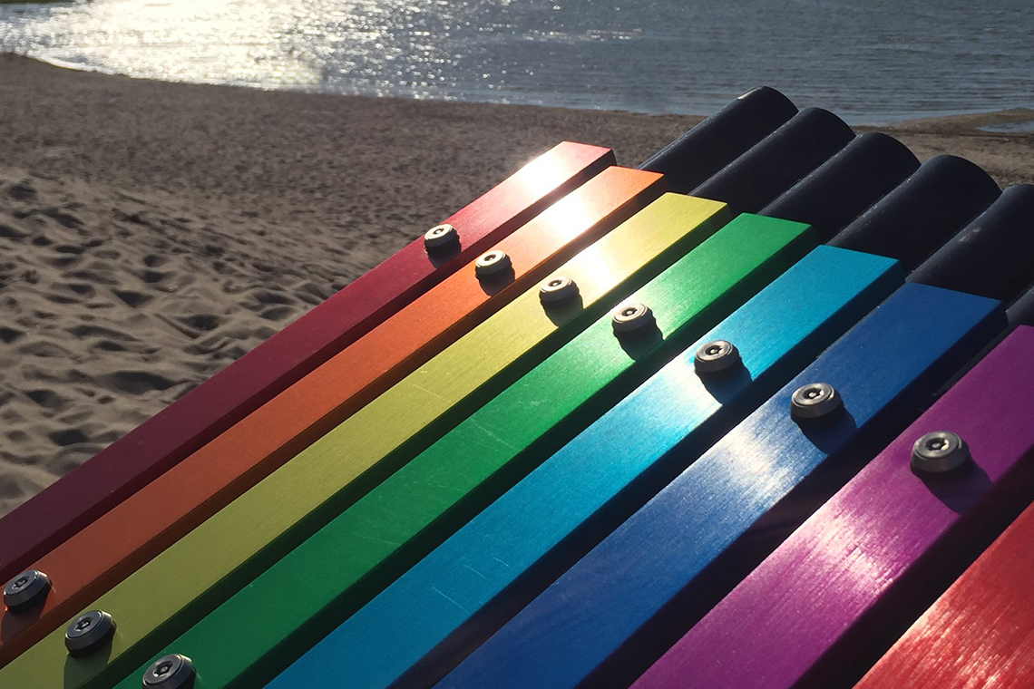 rainbow colored musical notes on an outdoor xylophone with a beach in the background