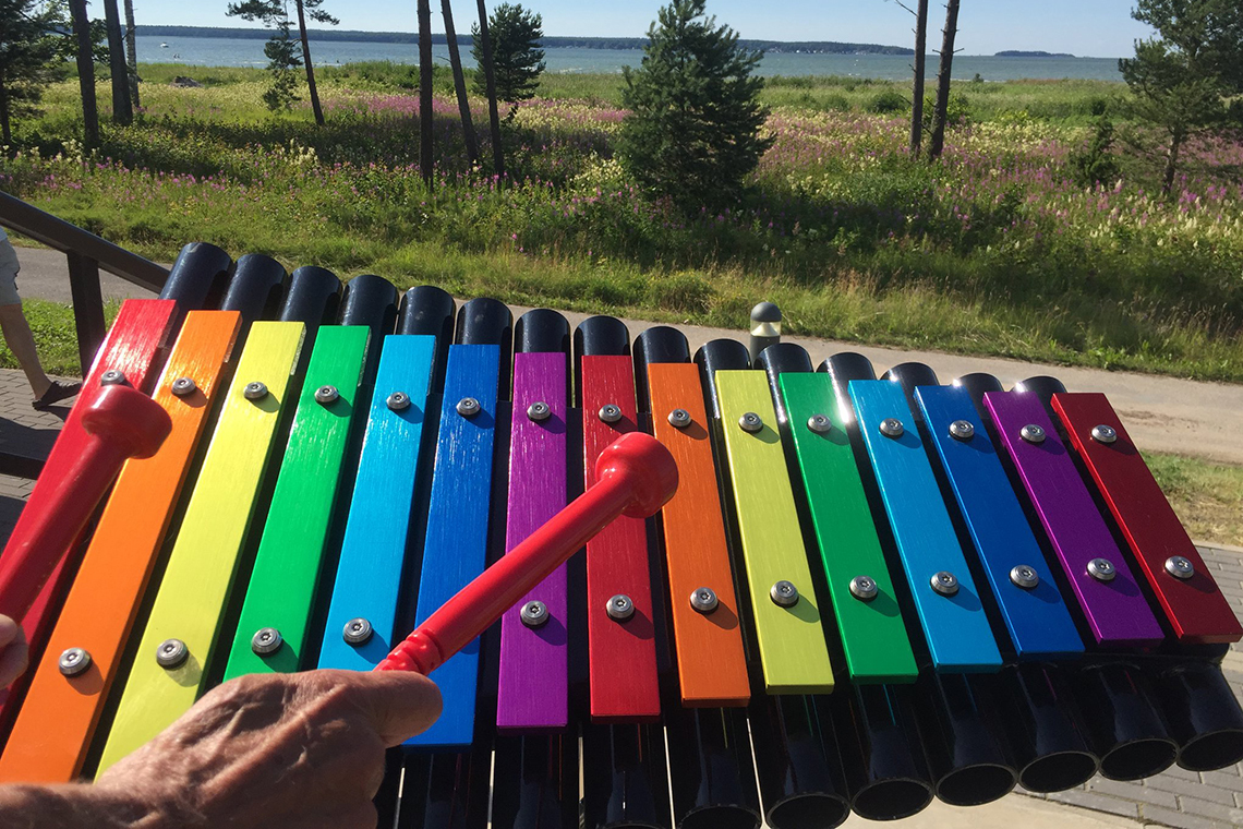 rainbow colored musical notes on an outdoor xylophone with a trees and the sea in the background