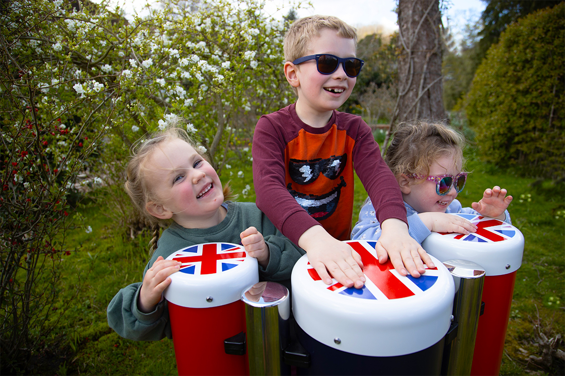three young children playing red white and blue outdoor conga drums