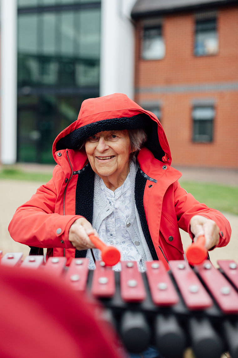 a senior lady wearing a red coat playing a large outdoor xylophone